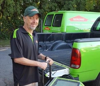 A photo of a smiling male employee wearing a black SERVPRO shirt standing in front of green SERVPRO trucks