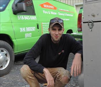 Male employee posing with HVAC cleaning equipment outside office with ServPro branded van in background. 