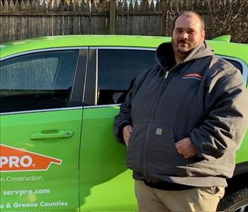 A photo of a smiling male employee in a grey SERVPRO® jacket standing in front of a green SERVPRO vehicle